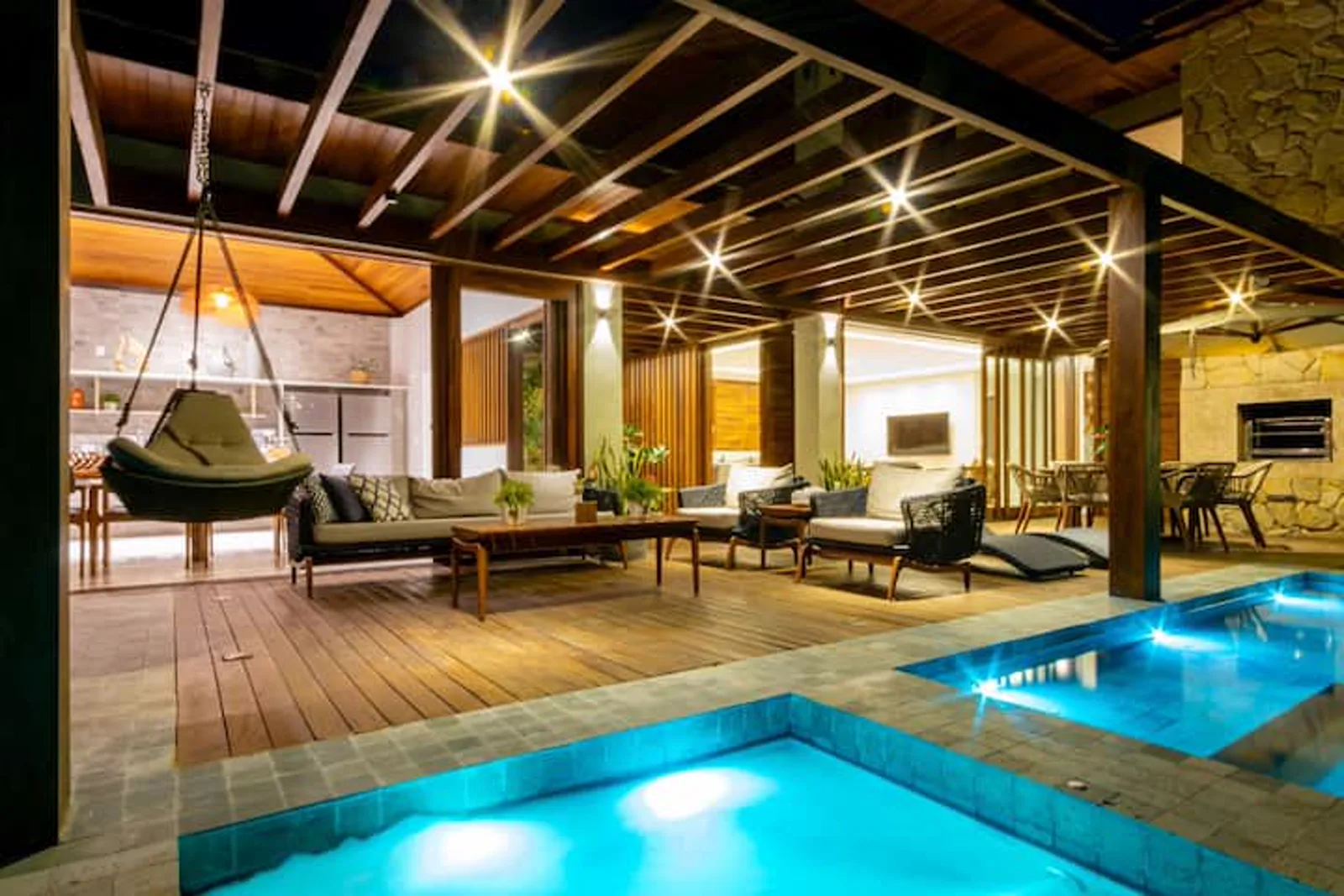 Deck coberto com poltrona suspensa, de frente para a piscina à noite