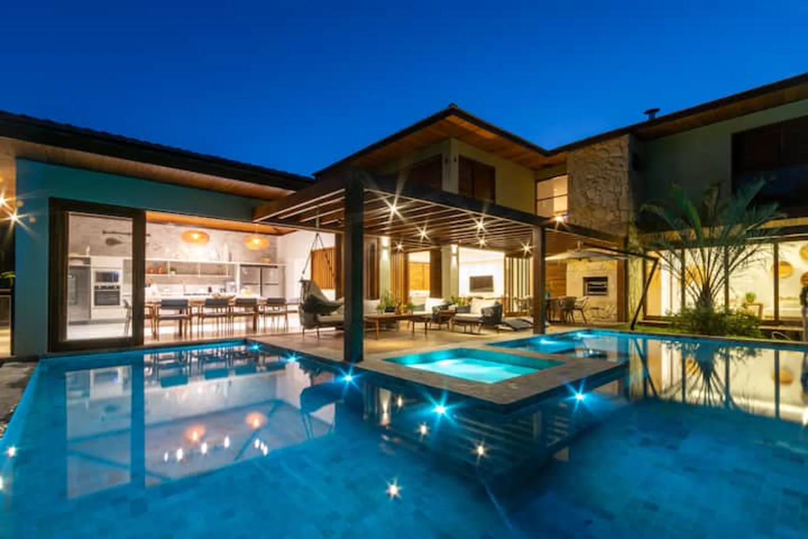Piscina com jacuzzi iluminada na hora azul, de frente para a casa