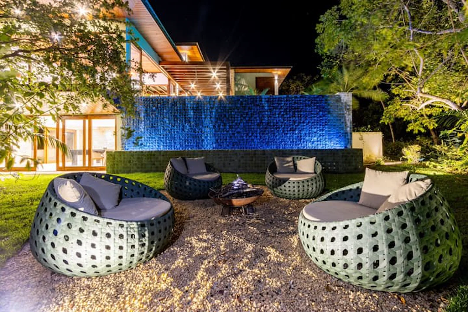 Lounge com fogueira e poltronas, sob a parede-cascata iluminada, à noite