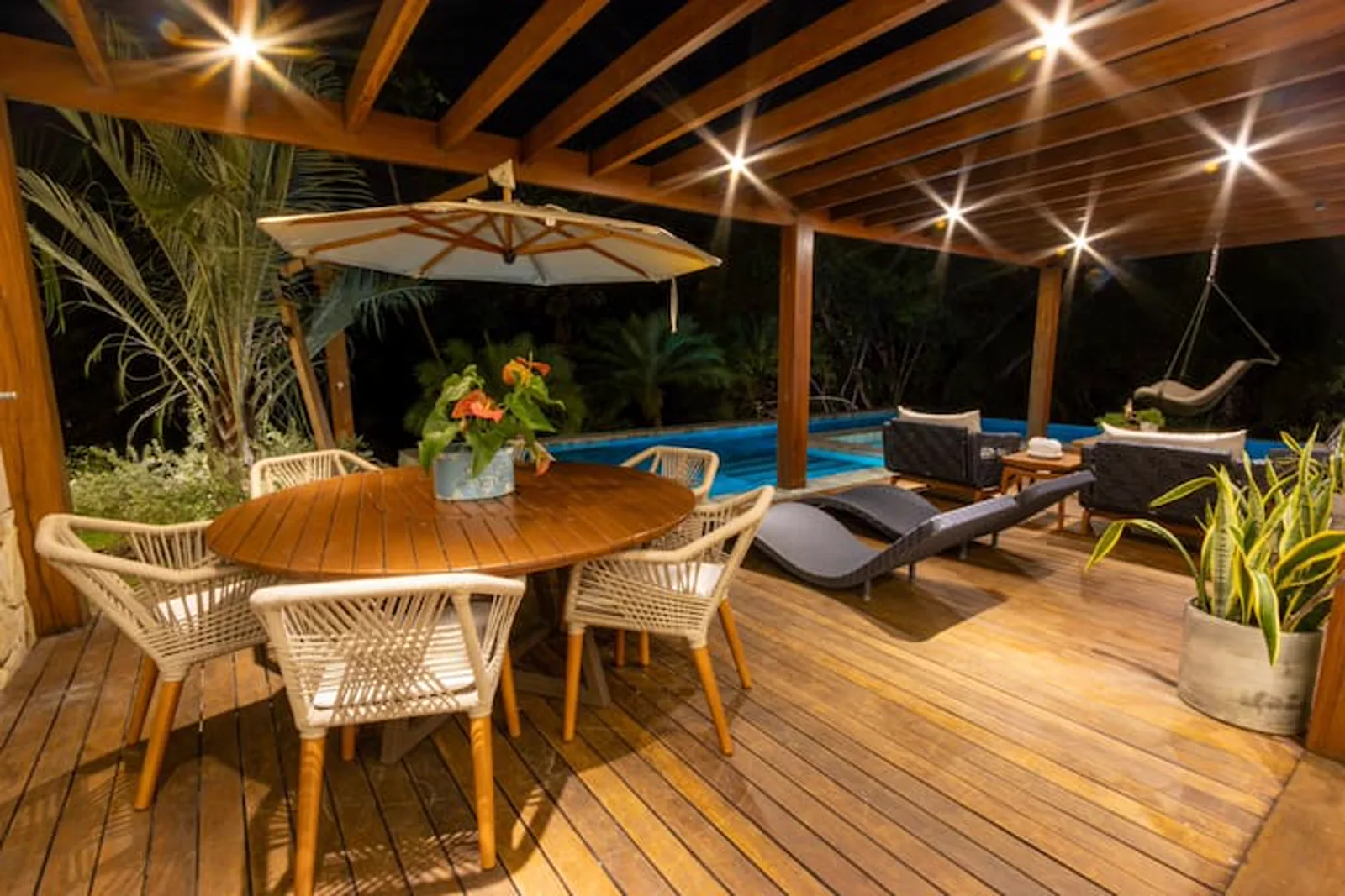 Deck coberto com mesa de jantar e a piscina, à noite