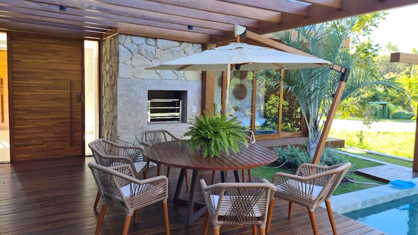 Espaço gourmet com churrasqueira e mesa de jantar, de frente para a piscina