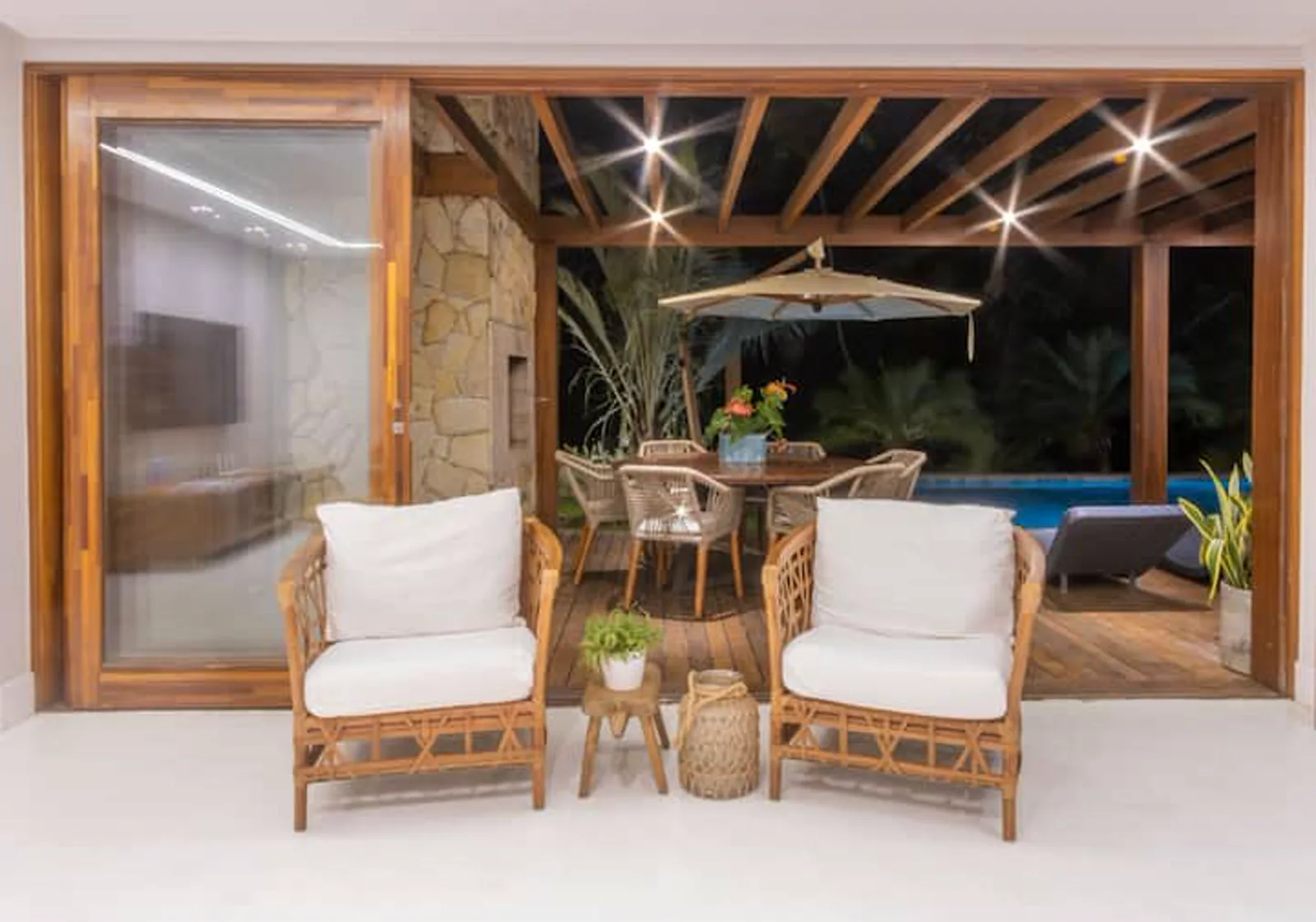 Varanda com poltronas de fibra e a piscina ao fundo, à noite